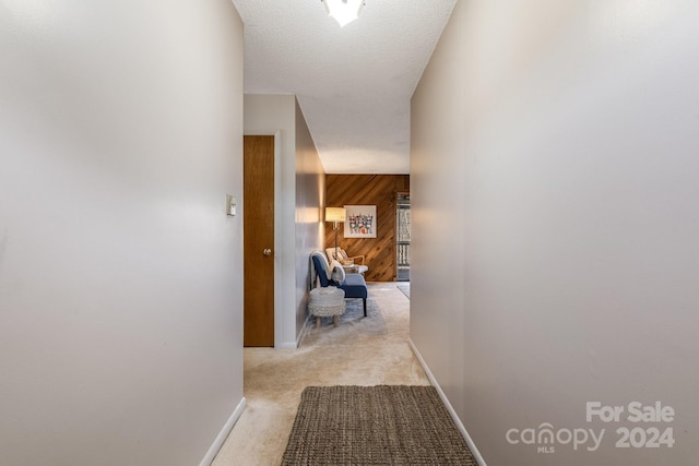 corridor featuring light carpet, a textured ceiling, and wood walls