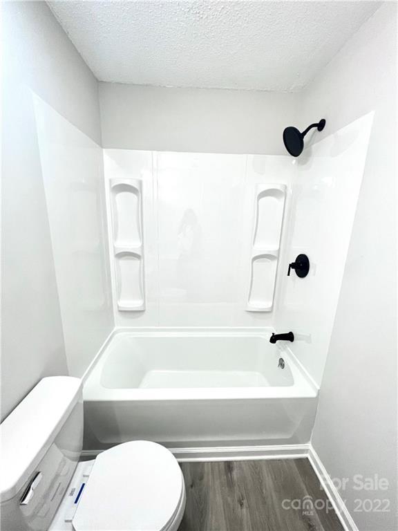 bathroom with washtub / shower combination, toilet, a textured ceiling, and hardwood / wood-style flooring