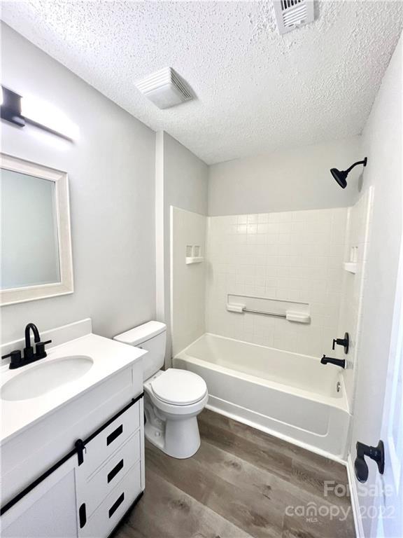 full bathroom with hardwood / wood-style floors, tiled shower / bath combo, a textured ceiling, toilet, and vanity