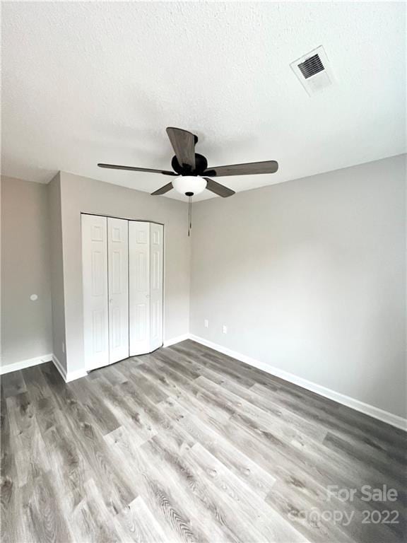 unfurnished bedroom featuring ceiling fan, a textured ceiling, dark wood-type flooring, and a closet