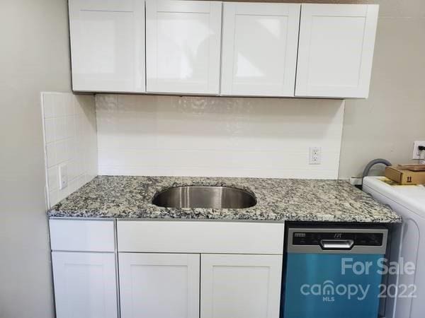 kitchen with washer / dryer, sink, white cabinets, stainless steel dishwasher, and light stone counters