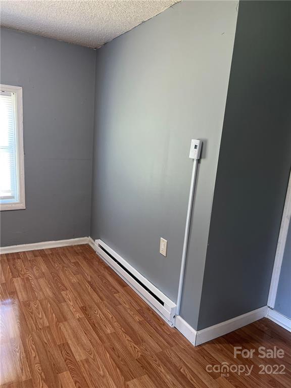 empty room featuring baseboard heating, a textured ceiling, and hardwood / wood-style flooring