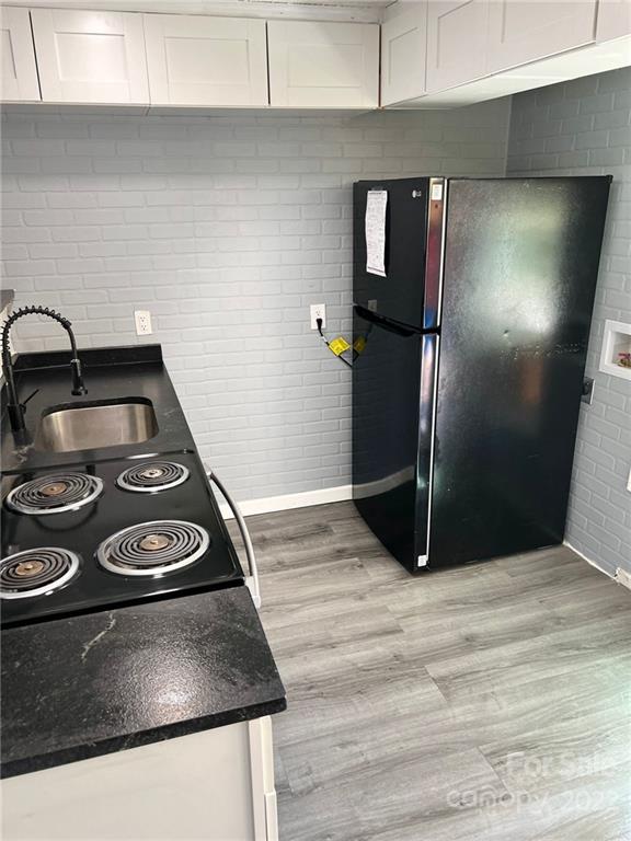 kitchen with sink, white cabinetry, light hardwood / wood-style floors, and black fridge