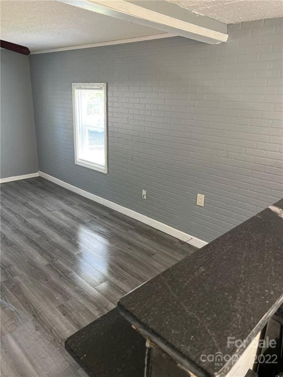 empty room featuring brick wall, dark wood-type flooring, and a textured ceiling