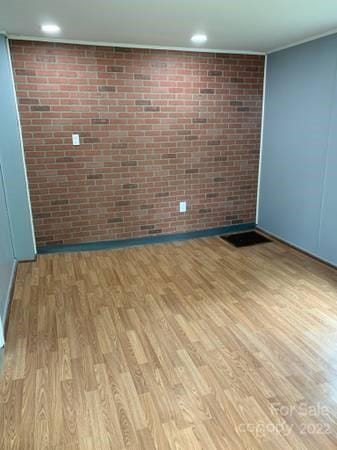 unfurnished room featuring brick wall and light wood-type flooring