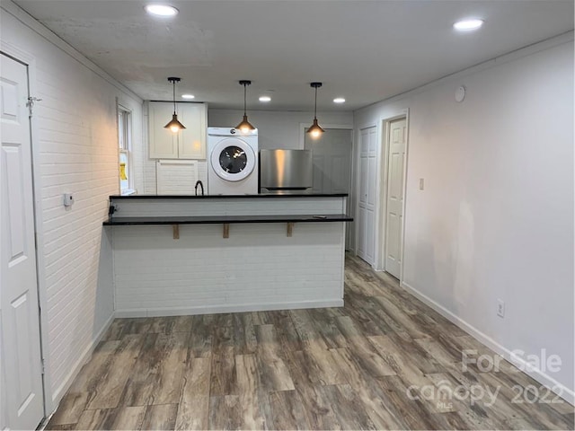 kitchen featuring pendant lighting, a kitchen bar, washer / clothes dryer, fridge, and dark hardwood / wood-style floors