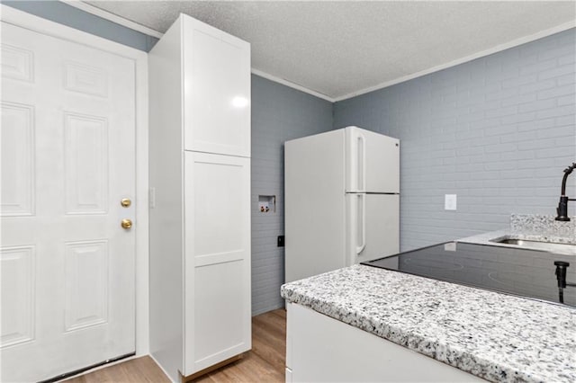 kitchen featuring white refrigerator, light stone counters, light hardwood / wood-style floors, and white cabinets