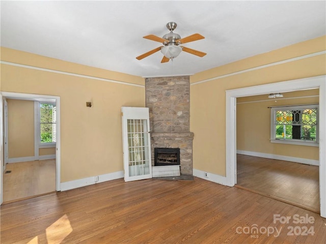 unfurnished living room featuring ceiling fan, light hardwood / wood-style flooring, and a stone fireplace