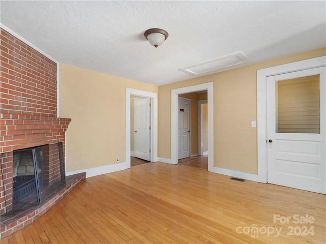 unfurnished living room with brick wall, a brick fireplace, a textured ceiling, and light wood-type flooring