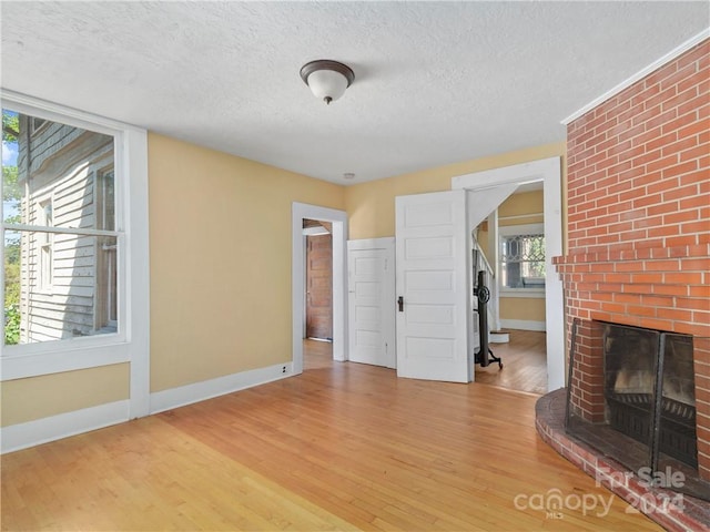 unfurnished living room with brick wall, light wood-type flooring, a fireplace, and a textured ceiling