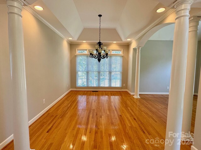 unfurnished dining area featuring hardwood / wood-style floors, a tray ceiling, ornamental molding, and a notable chandelier