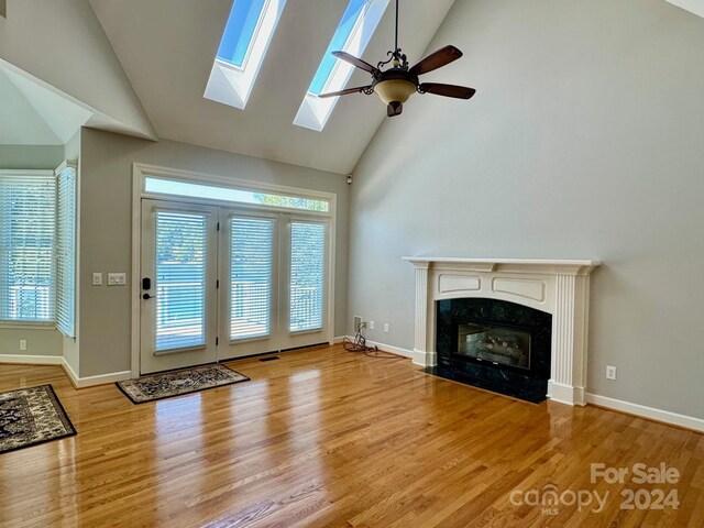 unfurnished living room with light wood-type flooring, a skylight, ceiling fan, high vaulted ceiling, and a premium fireplace