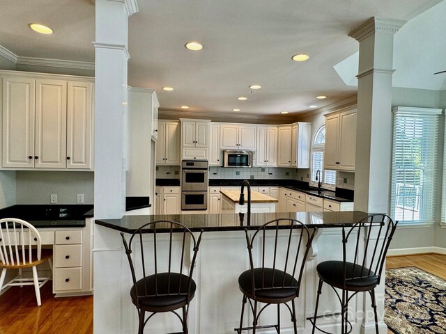 kitchen with appliances with stainless steel finishes, dark hardwood / wood-style floors, ornamental molding, and a kitchen breakfast bar