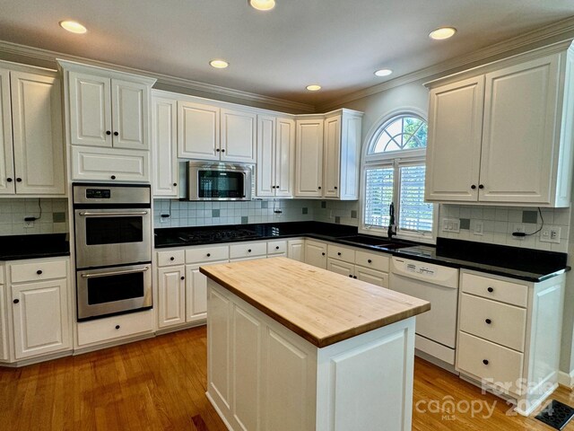 kitchen with white cabinets, light hardwood / wood-style floors, ornamental molding, and stainless steel appliances