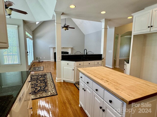 kitchen with ornate columns, white cabinets, vaulted ceiling, and light wood-type flooring