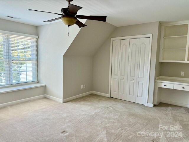 additional living space featuring built in shelves, ceiling fan, light colored carpet, and vaulted ceiling