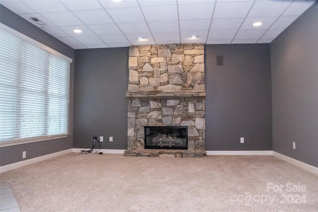 unfurnished living room featuring carpet flooring, a stone fireplace, and a paneled ceiling