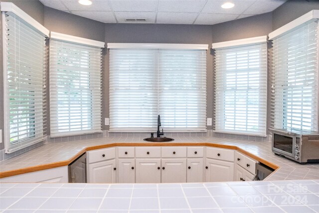 kitchen with tile counters, plenty of natural light, white cabinets, and sink