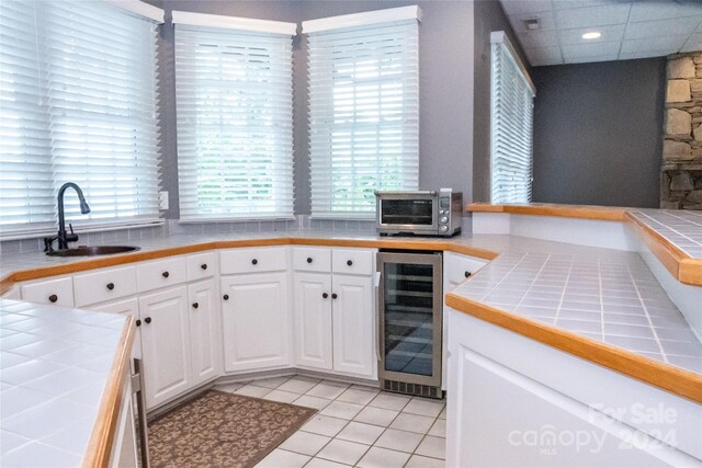 kitchen featuring a healthy amount of sunlight, white cabinetry, tile counters, and beverage cooler