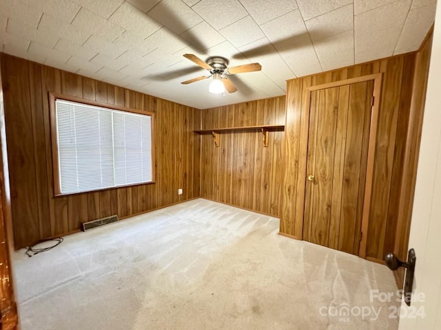 carpeted spare room featuring wood walls and ceiling fan