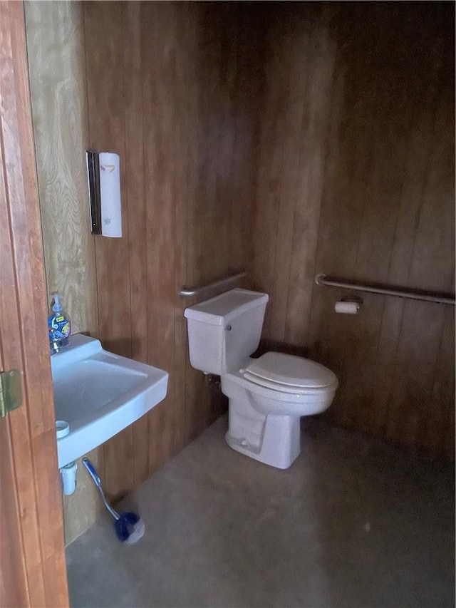 bathroom featuring toilet, wood walls, concrete flooring, and sink