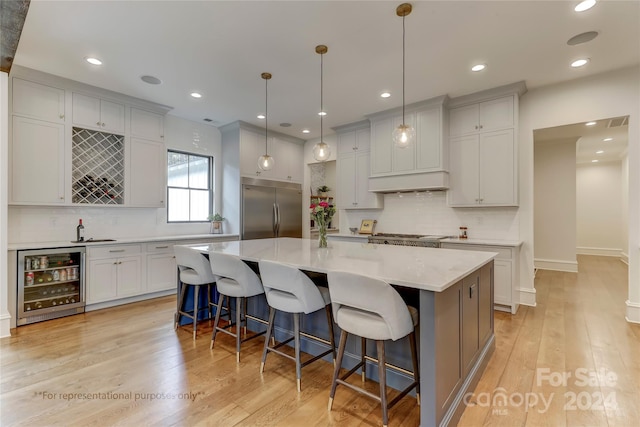 kitchen with stainless steel built in fridge, wine cooler, light hardwood / wood-style floors, and a center island