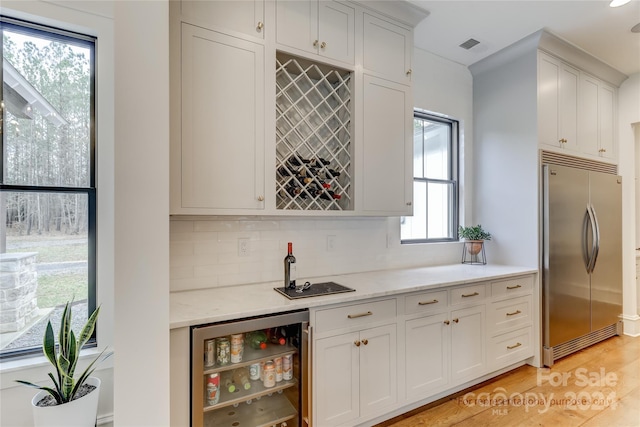 kitchen with beverage cooler, light hardwood / wood-style flooring, tasteful backsplash, and refrigerator