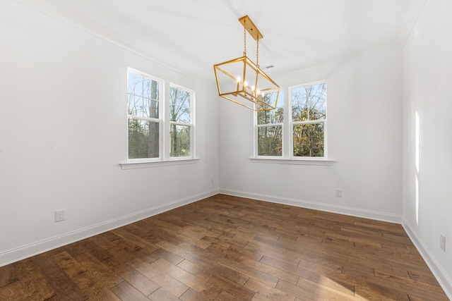 spare room featuring a chandelier, ornamental molding, and dark wood-type flooring