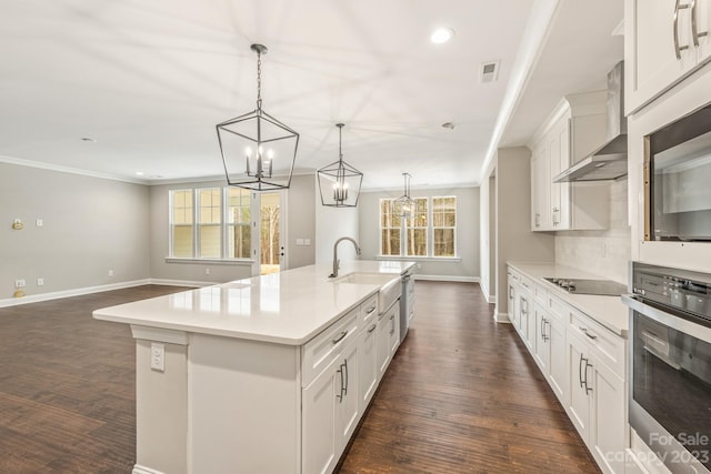 kitchen featuring dark hardwood / wood-style floors, a kitchen island with sink, wall chimney range hood, an inviting chandelier, and stainless steel oven