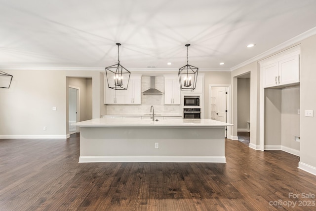 kitchen featuring dark wood-type flooring, a center island with sink, wall chimney range hood, and pendant lighting