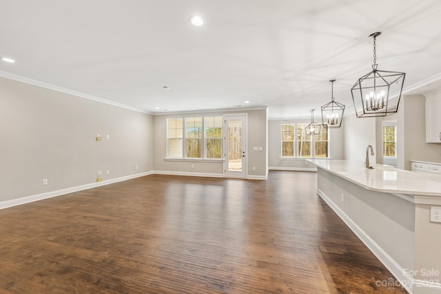 unfurnished living room featuring a wealth of natural light, an inviting chandelier, and dark hardwood / wood-style flooring