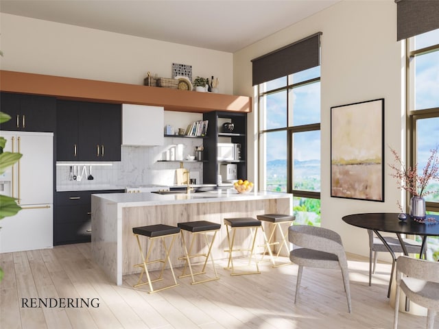 kitchen with backsplash, light wood-type flooring, an island with sink, and white refrigerator