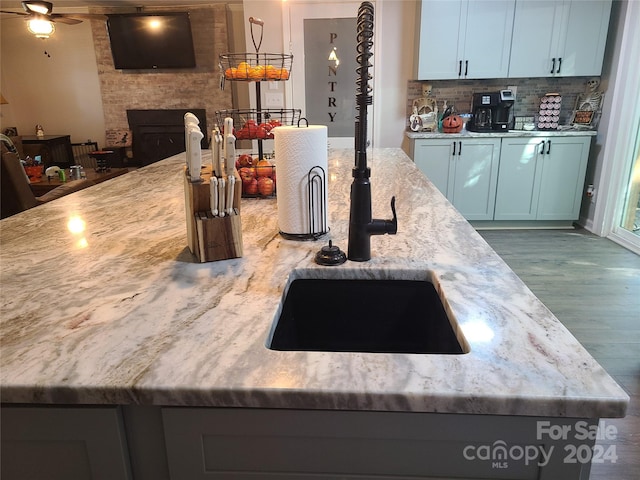 kitchen featuring a stone fireplace, ceiling fan, light stone countertops, hardwood / wood-style floors, and tasteful backsplash