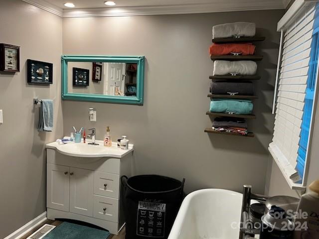 bathroom featuring vanity with extensive cabinet space, a washtub, and ornamental molding