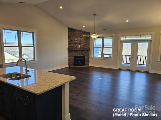 kitchen with light stone countertops, a center island with sink, vaulted ceiling, and dark hardwood / wood-style flooring