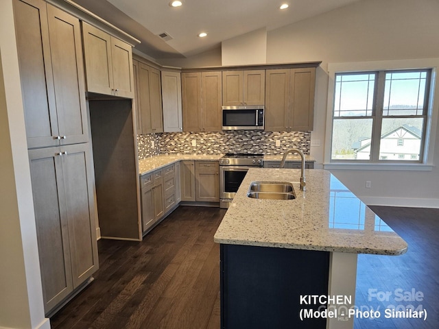 kitchen with a kitchen island with sink, dark wood-type flooring, stainless steel appliances, light stone countertops, and vaulted ceiling