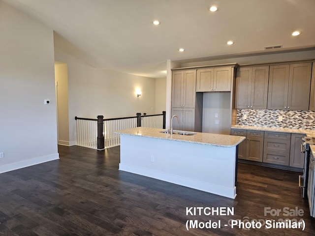 kitchen with light stone countertops, backsplash, a kitchen island with sink, dark hardwood / wood-style floors, and sink