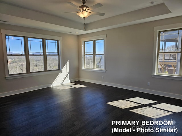 unfurnished room featuring a raised ceiling, plenty of natural light, dark hardwood / wood-style floors, and ceiling fan