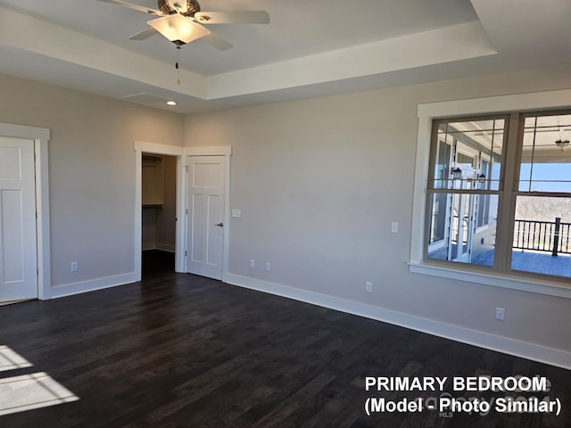 unfurnished room featuring a raised ceiling, ceiling fan, and dark hardwood / wood-style flooring