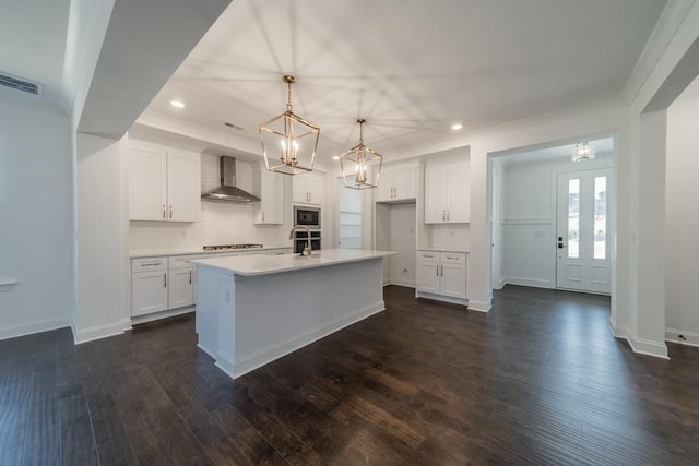 kitchen with white cabinets, an island with sink, dark hardwood / wood-style floors, and wall chimney range hood