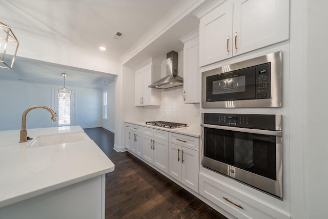 kitchen featuring white cabinetry, dark wood-type flooring, stainless steel appliances, wall chimney range hood, and tasteful backsplash