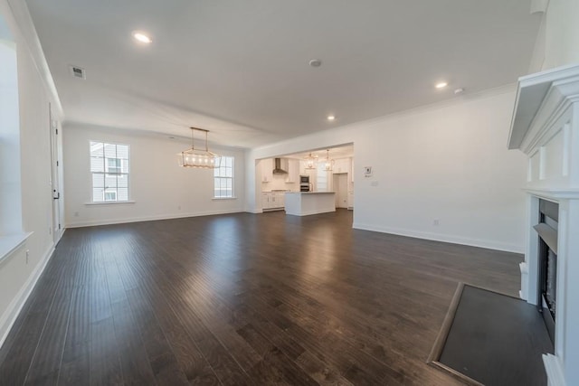 unfurnished living room featuring an inviting chandelier, dark hardwood / wood-style floors, and ornamental molding