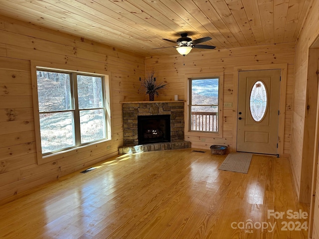 unfurnished living room featuring wooden ceiling, a fireplace, light wood-type flooring, wooden walls, and ceiling fan