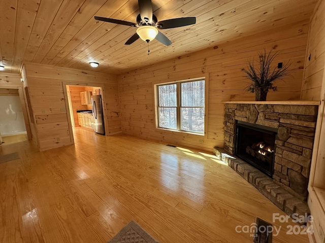 unfurnished living room with ceiling fan, wood ceiling, light hardwood / wood-style floors, wood walls, and a stone fireplace