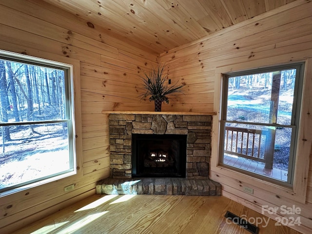 unfurnished living room featuring wood-type flooring, wood walls, and a stone fireplace