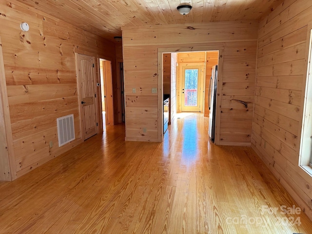 spare room with light wood-type flooring, wood ceiling, and wood walls