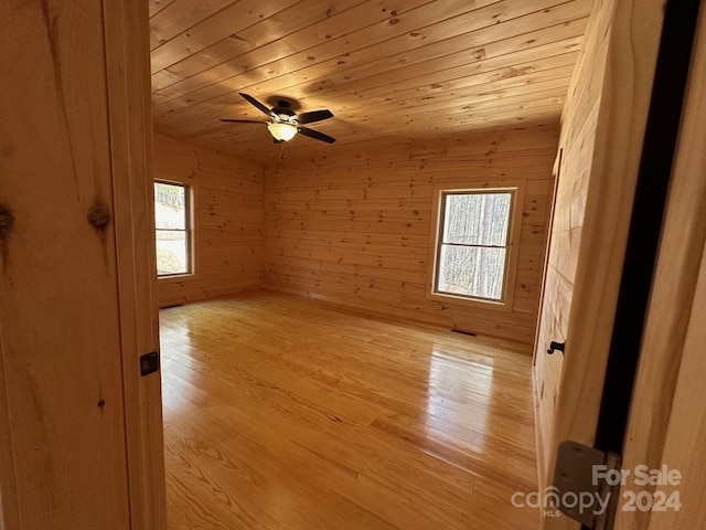 empty room with wood walls, ceiling fan, and light wood-type flooring