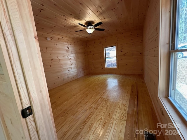 unfurnished room featuring wooden ceiling, wood walls, a skylight, light hardwood / wood-style flooring, and ceiling fan