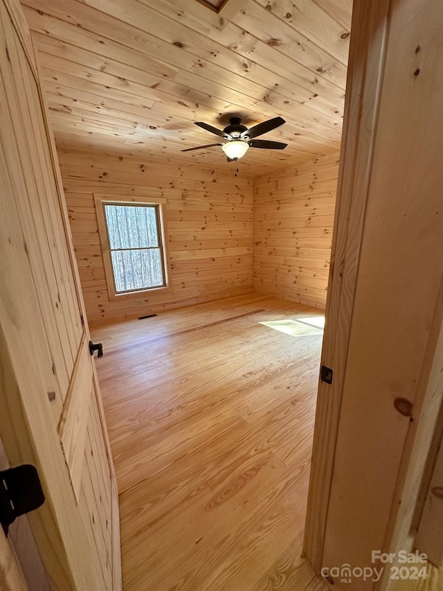 unfurnished room featuring wooden walls, wooden ceiling, ceiling fan, and light wood-type flooring