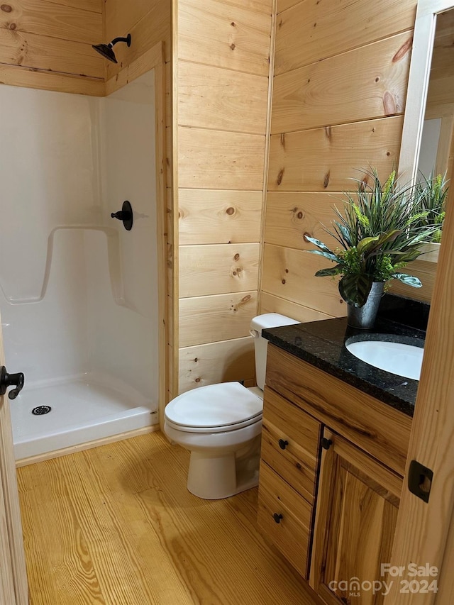 bathroom featuring a shower, wood-type flooring, wood walls, toilet, and vanity with extensive cabinet space